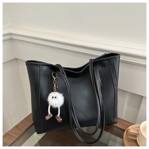 Detail of black faux leather tote bag featuring a cute white plush monster charm