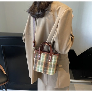 Detail of wool plaid bucket bag with brown leather handles and adjustable shoulder strap