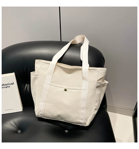 Detail of off-white canvas tote bag with bronze snap button pocket and side pockets