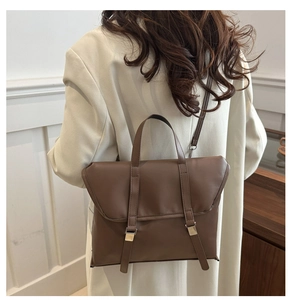 Detailed back view of a dark brown vintage briefcase bag carried by a model in a beige suit