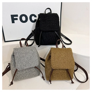 Trois sacs à dos en peluche noir, gris et marron sur un support d'exposition minimaliste