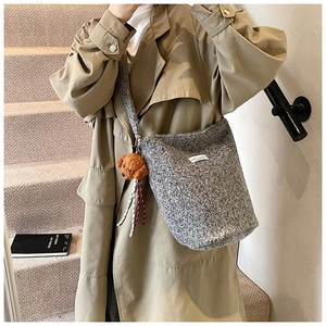 Close-up of grey wool bucket bag with cute brown teddy bear charm and soft strap