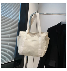 Detail of off-white canvas tote bag featuring metal snap buttons and functional side pockets