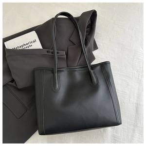 Close-up of black faux leather tote bag with decorative stitching on white fabric