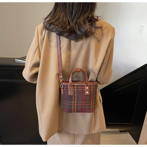 Detail of red and green plaid woolen bucket bag with brown leather strap and gold ring buckle