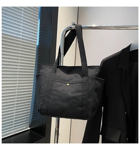 Detail of minimalist black canvas tote bag featuring a vintage gold snap button and side pocket
