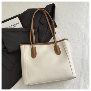 Detail of off-white tote bag with brown handles on grey suit and white textured background