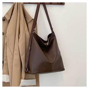 Close-up of deep brown tote bag with vintage leather texture hanging on a wooden hook