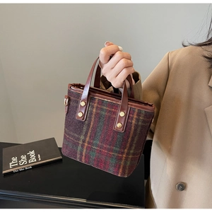 Detail of red and green plaid wool tote with brown leather handles and gold rivets
