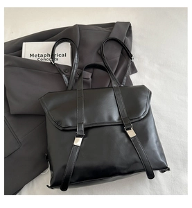 Flat lay of a black vintage PU leather briefcase backpack with metal buckles on white fabric
