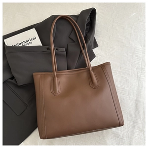 Detailed top view of a large brown leather tote bag on textured white fabric and blazer