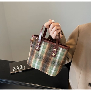 Detail of green plaid wool tote bag with brown leather handles and gold rivet accents