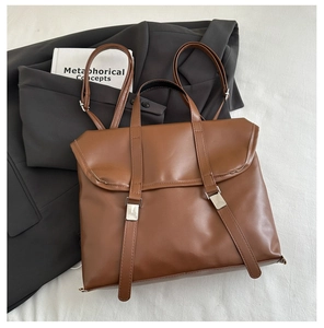 Detail of a brown leather satchel with metal buckles on a minimalist white fabric background