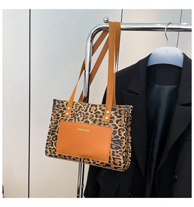 Detail of leopard print tote bag featuring a brown leather outer pocket and double straps