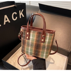 Close-up of retro plaid woolen bucket bag with brown leather handles in a gift box