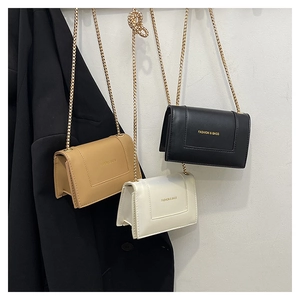 Close-up of minimalist leather flap bag with gold chain strap and metal lettering