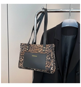 Close-up of leopard print tote bag featuring a black leather patch with gold text