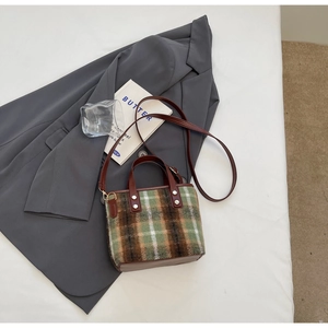 Retro wool plaid bucket bag detail with brown leather handle and silver studs on white background
