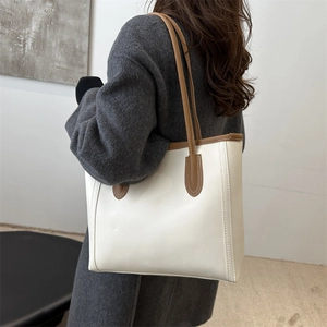 Minimalist beige leather tote bag with brown trim shown on shoulder for commuting