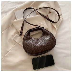 Detailed close-up of dark brown crescent bag with woven texture on beige clothing background