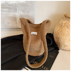 Detail of a brown fuzzy bucket bag with white logo label against a black blazer background
