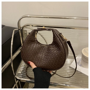 Detail of dark brown woven crescent bag with leather texture and golden metal hardware