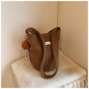 Detail of coffee brown wool bucket bag with cute bear charm on white textured background