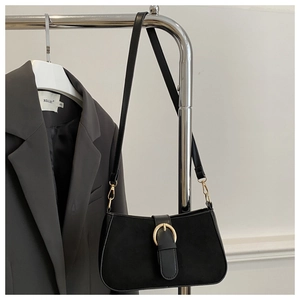 Detail of matte black suede shoulder bag featuring a gold buckle on grey blazer backdrop