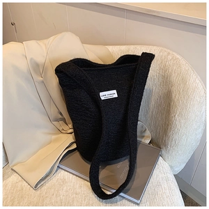Detail of black faux shearling bucket bag with white patch on cozy armchair