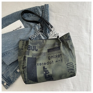 Close-up of newspaper print tote bag with vintage gray-green finish and black leather straps