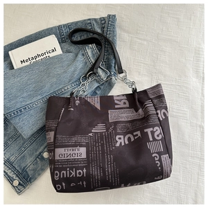 Detailed view of newspaper print tote bag with silver chain strap on denim fabric