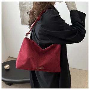 Detail view of burgundy suede tote bag with knotted strap and metal logo plaque