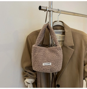 Close-up of brown plush bucket bag with CLEAR K logo hanging on khaki blazer