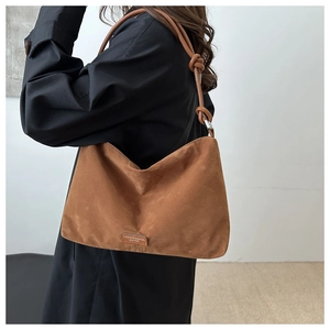 Detail of suede shoulder bag featuring a knotted leather strap and embossed brand label