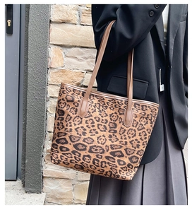 Close-up of leopard print tote bag with brown leather handles against a brick wall
