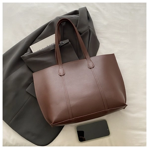 Detail view of large dark brown leather tote bag with vertical stitching on grey blazer