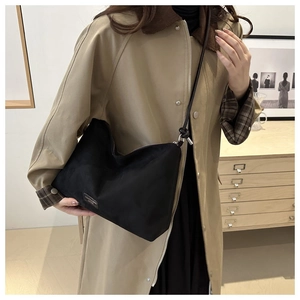 Detail of black suede hobo bag with fashion logo patch and zip closure on trench coat