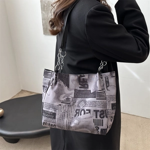 Chic newspaper print tote bag with silver chain strap shown from a side perspective