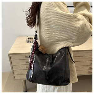 Detail of a soft black PU leather hobo bag with a plush pompom charm and woven rope accent