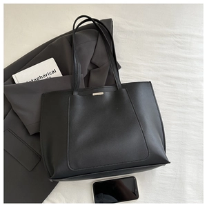 Detailed view of black faux leather tote bag with slender handles and metal plate detail