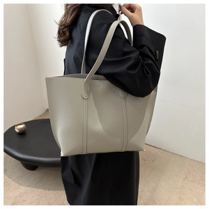 Detailed side view of a large light grey minimalist tote bag styled on a female model