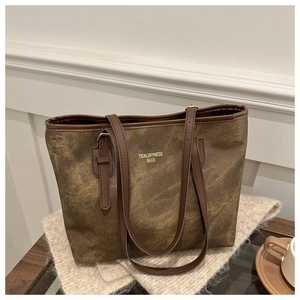 Dettaglio della borsa tote marrone vintage con logo dorato su morbida maglia beige