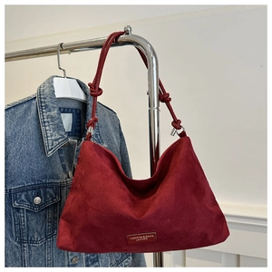 Close-up of dark red suede shoulder bag with knot strap detail and leather brand tag