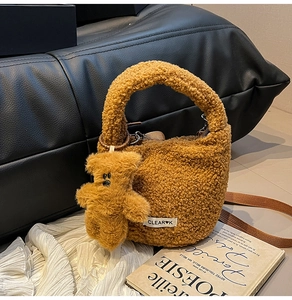 Detail of caramel brown faux shearling bucket bag with plush bear charm and woven label