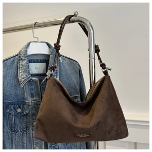 Detail of a brown suede hobo bag with sleek leather strap and front brand tag