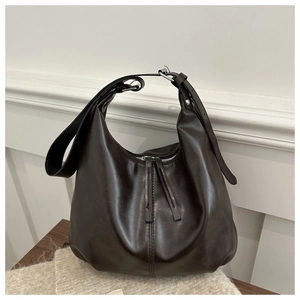 Detail of dark brown glossy leather Hobo bag with long tassel zippers on a wooden surface