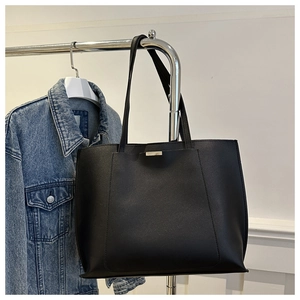 Detail of minimalist black PU leather tote bag with silver buckle hanging on metal rack