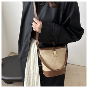 Chic beige and brown bucket bag with gold clasp shown on a model in a black trench coat