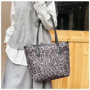 Detail of grey leopard print tote bag with black leather straps on model shoulder