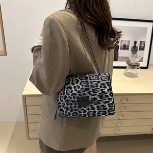 Chic leopard print crossbody bag with metallic chain strap worn in a cozy home setting